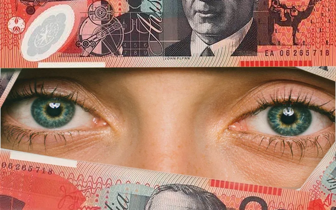 A close-up of a person's eyes peering between Australian banknotes.