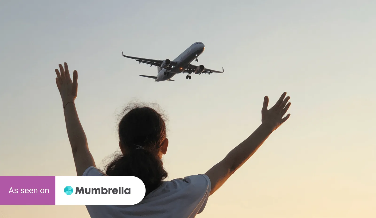 A child with arms raised watches an aeroplane fly overhead at sunset, with an 'As seen on Mumbrella' badge.