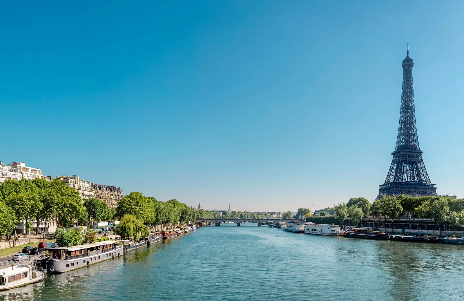 The Eiffel Tower rising above the River Seine, with boats moored along the water.