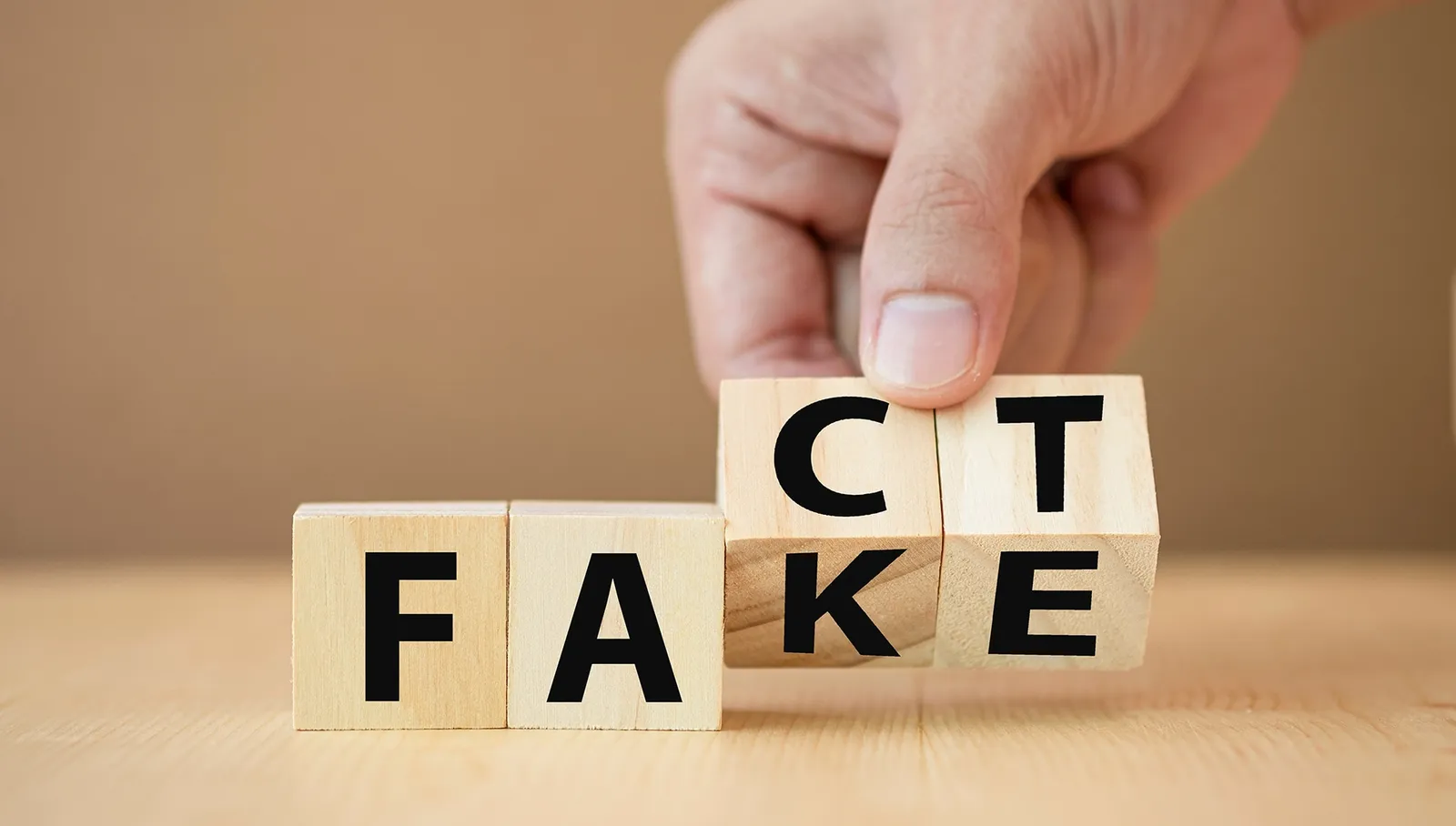 Wooden blocks being turned to change the word 'FAKE' into 'FACT'.