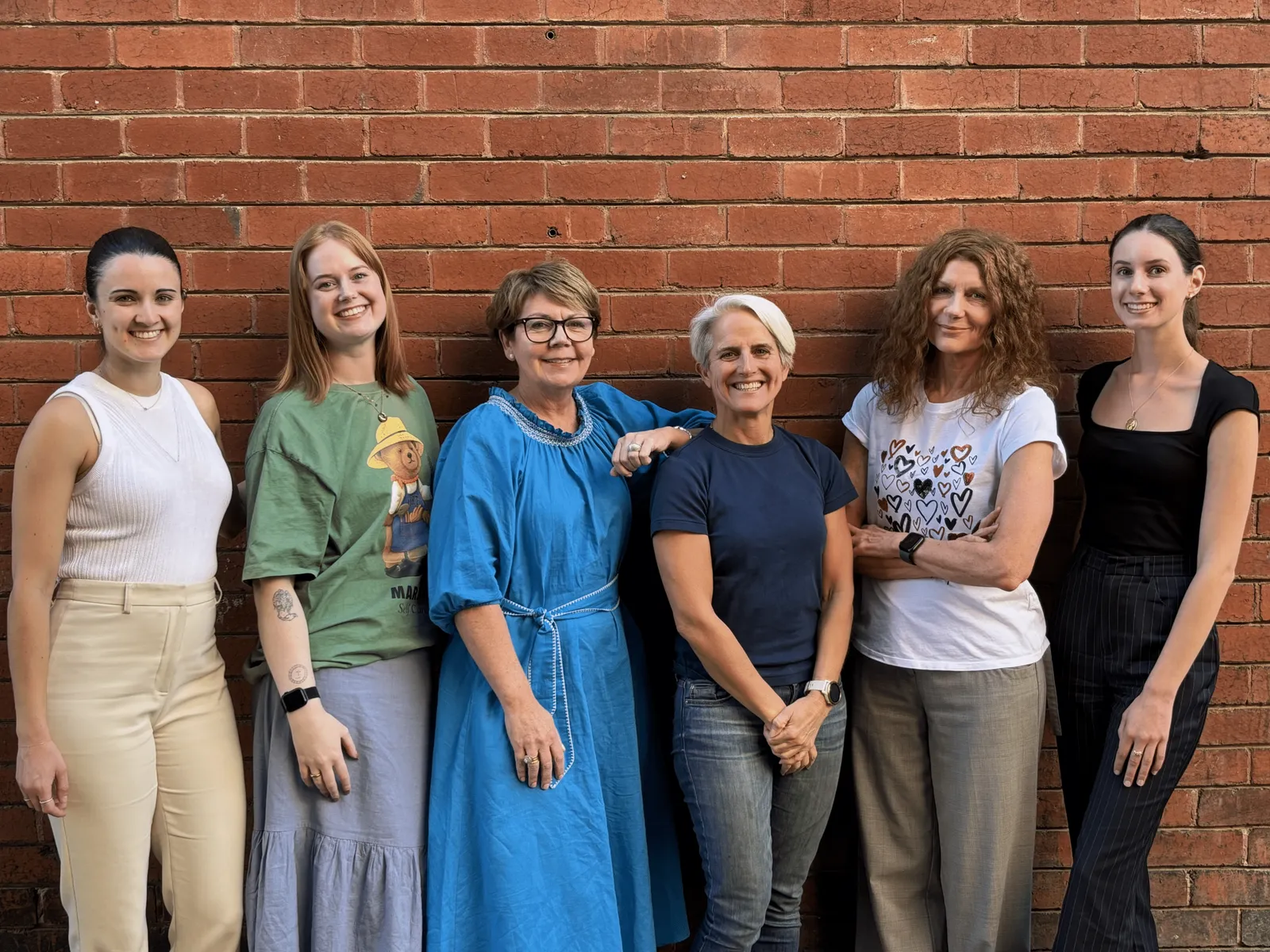 Six women stand smiling in front of a brick wall.