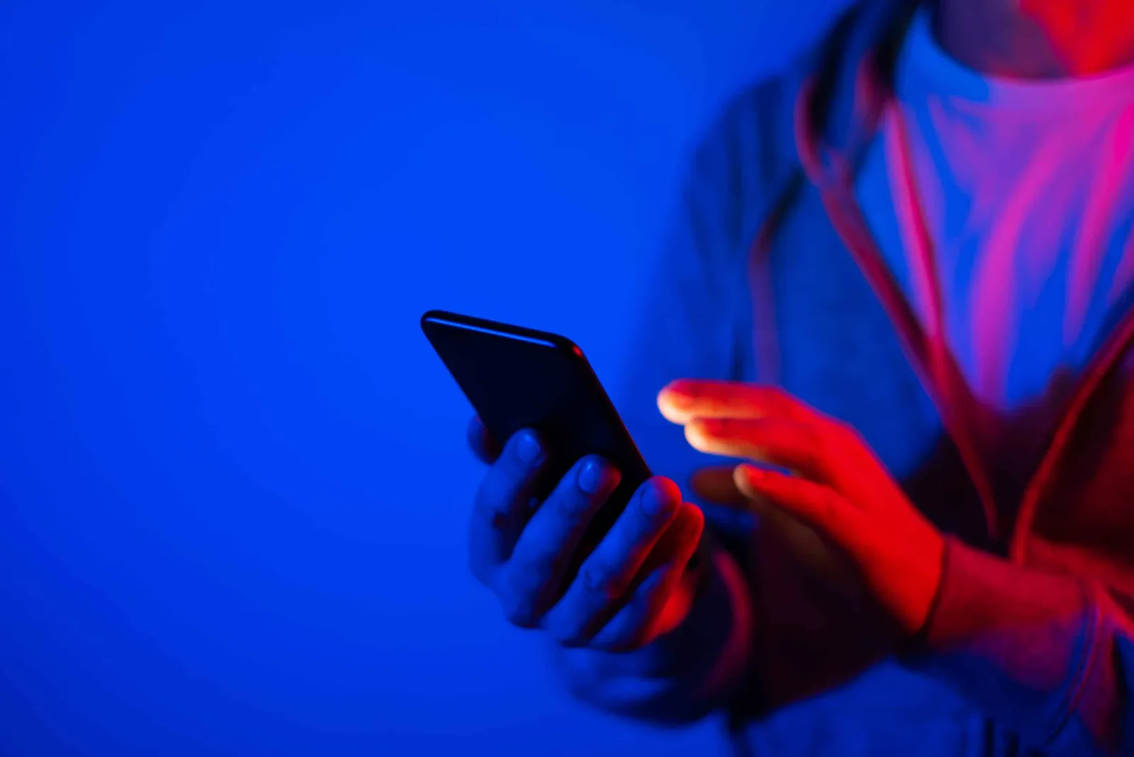 A person holds a smartphone in blue and red light.