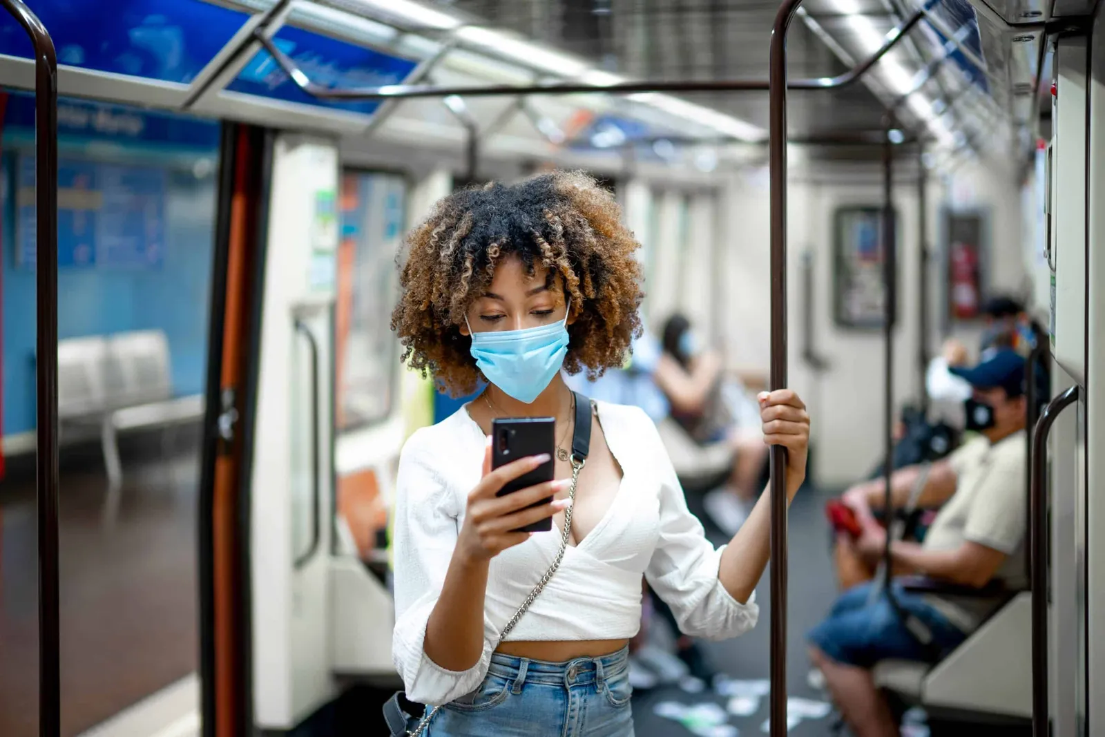A woman in a face mask checks her phone on a train.