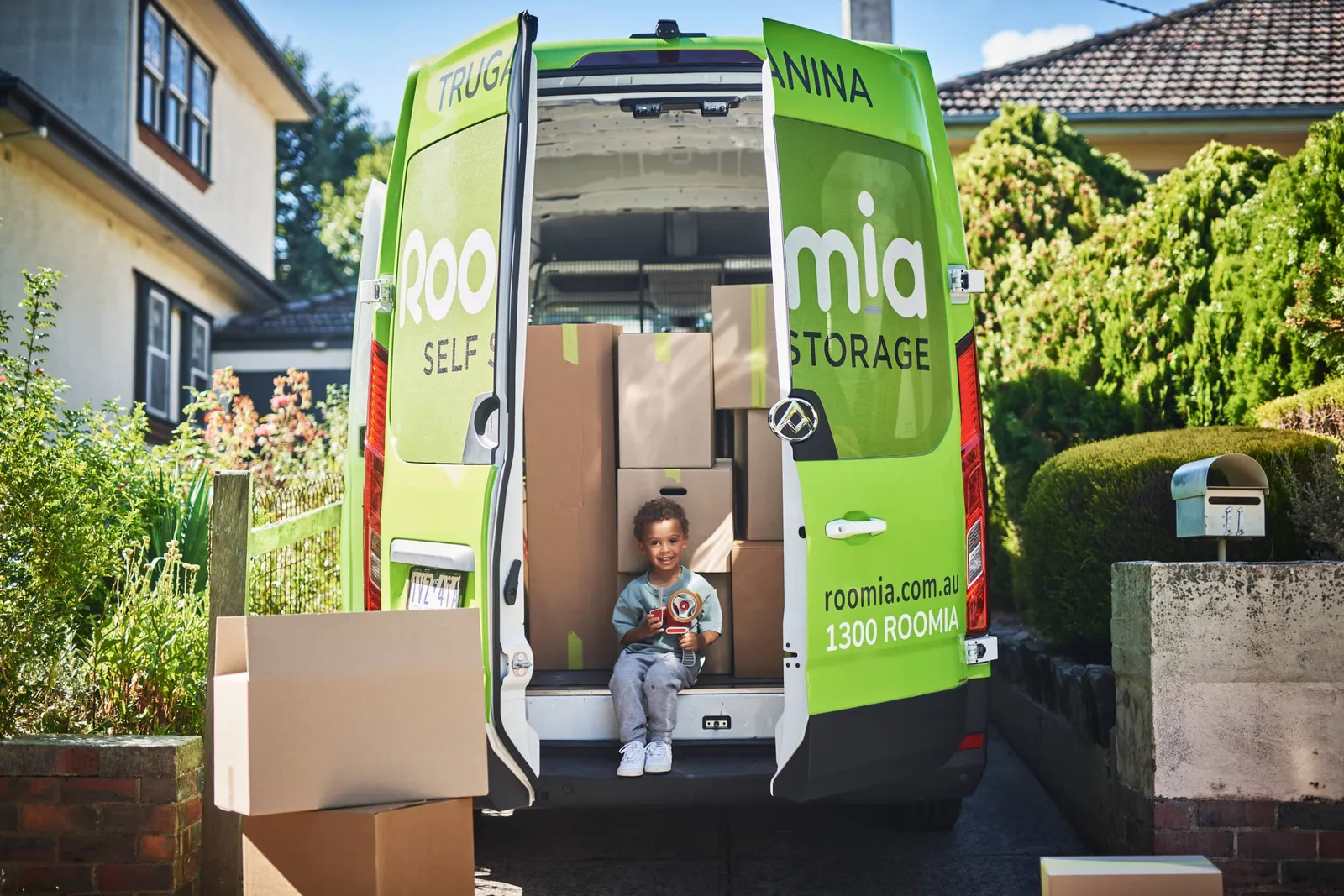 A Roomia self storage van with its back doors open and a child sitting inside among boxes.